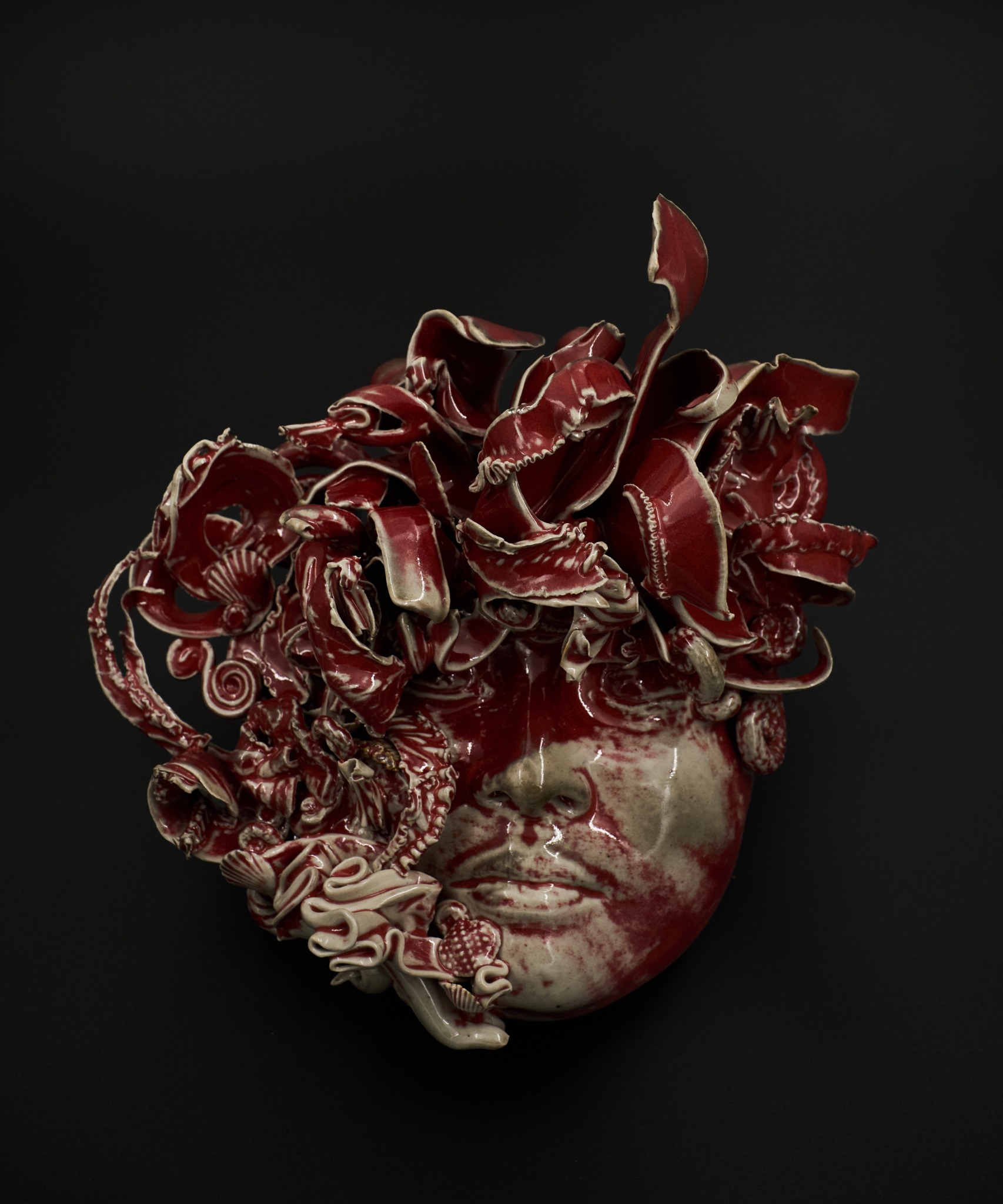 Red glazed ceramic face surrounded by sweeping curls and layered organic forms, by Chia Hwu